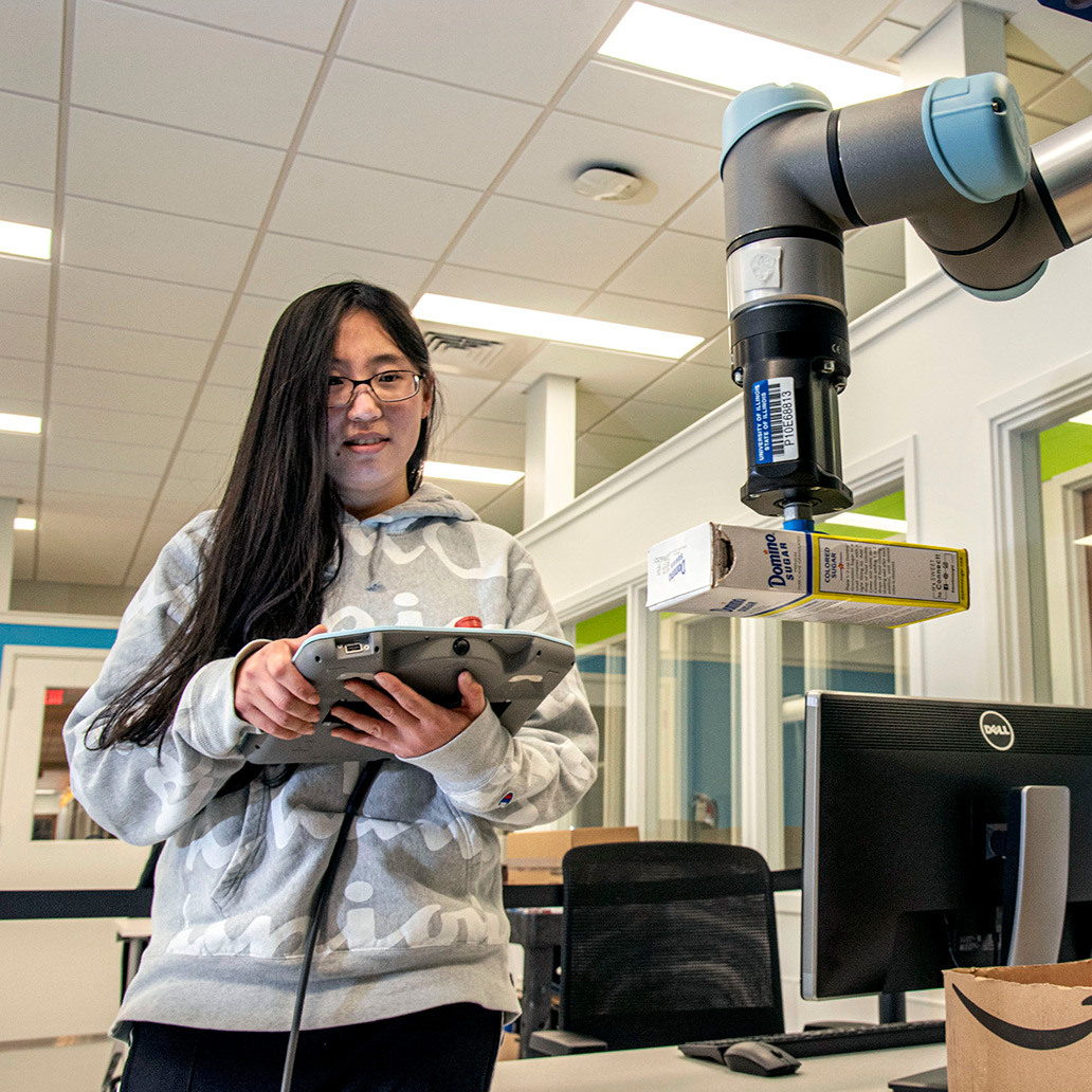 a female engineering student working with a robotic packaging arm